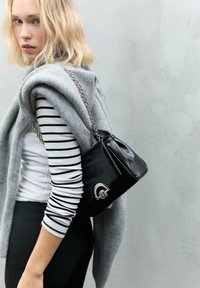 Schwarze Lederhandtasche mit silbernen Hardware-Details. Gestylt mit einem grauen Pullover, der über einem schwarz-weißen gestreiften Hemd getragen wird.