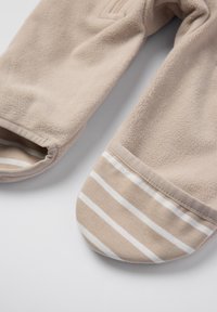 Fleece-fodrede design i beige, med en solid tekstur og stribet bomuldsforet ved foden. Inkluderer en detalje med lynlås.