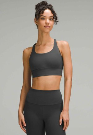 Crop top sportivo nero con spalline regolabili, abbinato a leggings neri a vita alta. Il materiale sembra liscio e aderente.