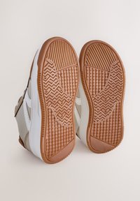 Baskets blanches et beige avec semelles en caoutchouc. Caractéristiques notables : semelle extérieure marron texturée et motif adhérent pour une meilleure traction.