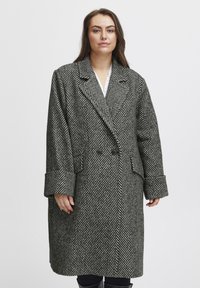 Cappotto a motivo spina di pesce in bianco e nero, dotato di colletto a rever, chiusura con bottoni doppi e ampi polsini.