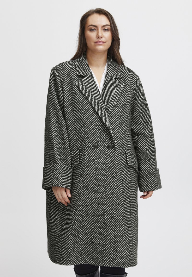 Cappotto a motivo spina di pesce in bianco e nero, dotato di colletto a rever, chiusura con bottoni doppi e ampi polsini.