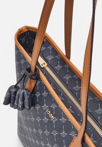 Granatowa torebka o teksturowym wykończeniu, z brązowymi skórzanymi akcentami, zamkiem błyskawicznym i subtelny wzorem. Posiada dekoracyjny chwost.