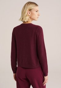 Pull en tricot bordeaux avec un motif texturé, col rond et manches longues. L'ourlet est légèrement court, associé à un pantalon assorti.
