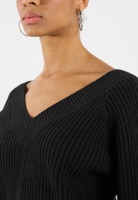 Schwarzer gerippter Pullover mit V-Ausschnitt. Das Material zeichnet sich durch ein strukturiertes Strickmuster aus, das seine weiche, flexible Struktur betont.