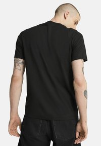 T-shirt in cotone nero con colletto rotondo e maniche corte, dal design semplice e dalla vestibilità comoda, vista dal retro che mostra i tatuaggi sulle braccia.