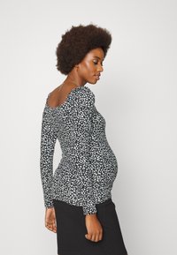 Camisola preta de mangas longas com pintas brancas, apresentando um decote amplo e um design ajustado, combinada com uma saia preta canelada.