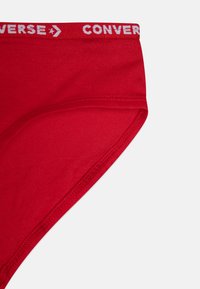 Κόκκινο βαμβακερό μπικίνι εσώρουχο με φαρδύ λευκό ελαστικό που φέρει εκτύπωση "CONVERSE" σε επαναλαμβανόμενο σχέδιο. Μαλακή υφή και εφαρμοστό σχέδιο.