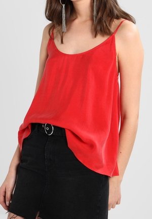 Mujer con una blusa roja sin mangas con tirantes finos combinada con una falda negra de talle alto y pendientes de aro plateados con flecos.