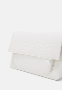 Väska i vitt läder med en strukturerad form, utrustad med ett klaffstängning och präglad logotyp på framsidan. Slät textur och minimalistisk design.