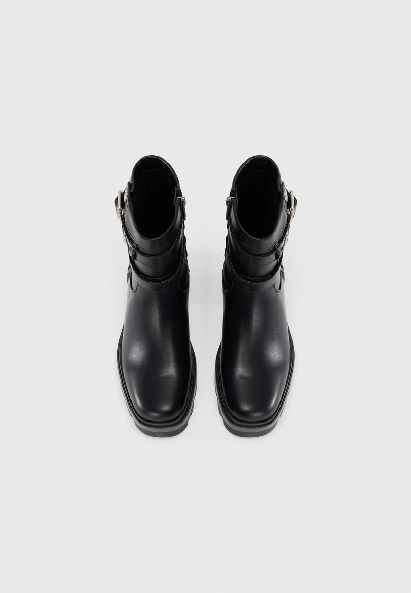 Botines negros con un acabado de cuero suave, punta redonda y detalles de hebilla. Presentan un tacón bajo apilado y cierre lateral con cremallera.