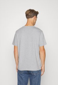 Camiseta de algodón gris con mangas cortas y cuello redondo, que presenta un corte holgado y una textura suave. Costuras visibles en las uniones.