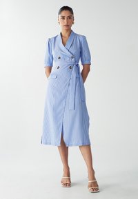 Robe portefeuille rayée bleu clair avec manches courtes bouffantes, fermeture à boutons double boutonnage, lien à la taille et poches latérales, atteignant la longueur mi-mollet.
