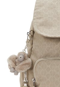Sac à dos beige à motifs avec des zips avant et un porte-clés gorille en peluche beige attaché à la tirette du zip latéral.