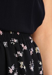 Jupe noire avec des motifs floraux en rose, jaune et blanc. Dispose d'une taille élastique et d'un tissu texturé.