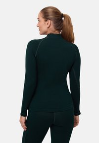 Maglietta a maniche lunghe verde scuro con colletto alto e cuciture piatte, abbinata a pantaloni coordinati. Texture liscia, design aderente.