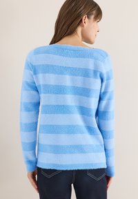 Maglione a maglia azzurro chiaro con ampie strisce orizzontali in tonalità scure e chiare. Tessuto morbido e scollo ampio, abbinato a jeans scuri.