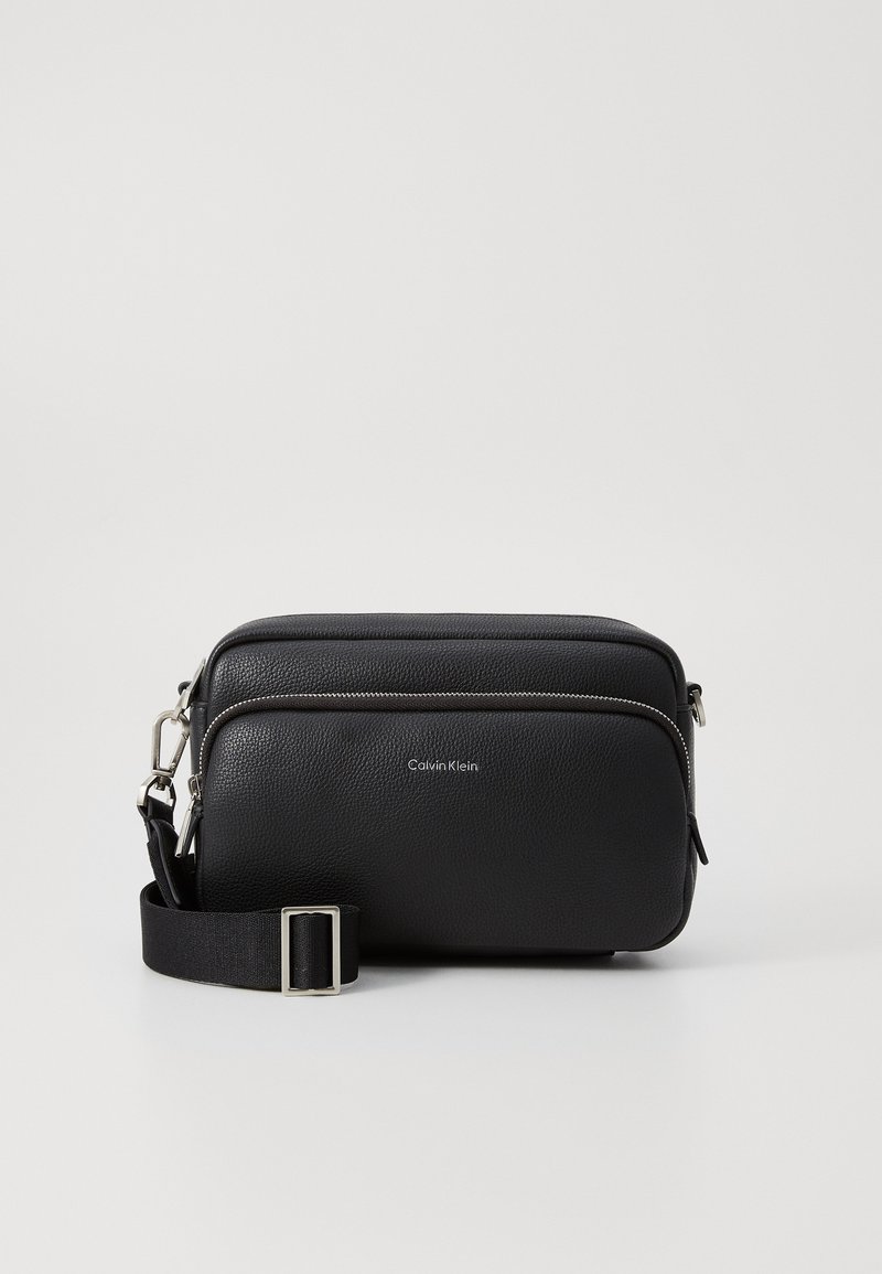 Borsa a tracolla nera in pelle con due scompartimenti con zip, finitura texturizzata, tracolla regolabile e dettagli in metallo argento. Logo di Calvin Klein visibile.