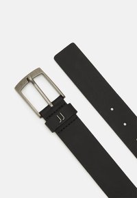 Ceinture en cuir noir avec une boucle rectangulaire en métal argenté et deux pointes métalliques. Elle présente des coutures soignées et plusieurs trous de réglage.