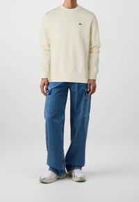 Krämmig, sweatshirt med rund halsringning och en liten grön logotyp. Matchas med lösa, baggy blå denim cargo byxor och vita sneakers.