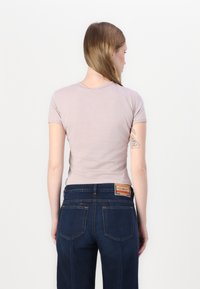 T-shirt fitted di un leggero color malva con maniche corte, abbinato a jeans denim blu scuro. La T-shirt presenta un collo semplice; i jeans hanno tasche posteriori e etichetta.