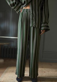 Grønstribet pyjamas sæt lavet af satin stof. Skjorten har en løs pasform med knapper, og bukserne har en vidde ben design.