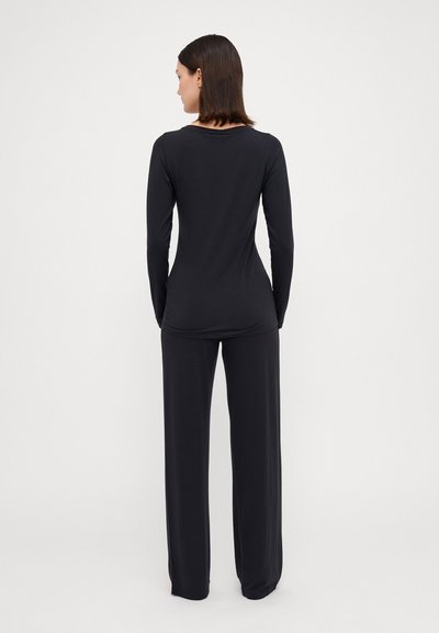 Camicia nera a maniche lunghe con collo rotondo, abbinata a pantaloni neri larghi, entrambi in un tessuto liscio e dal design minimalista.