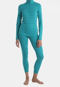 Türkisfarbenes Sportbekleidungsset mit einem Langarmoberteil mit halbem Reißverschluss und passenden Leggings, beide mit einem sich wiederholenden Logo-Muster und glatter Textur.