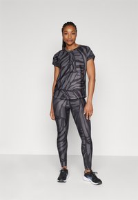 Svart treningstøy med en kortermet topp som har et subtilt stripet mønster og matchende tettsittende leggings. Materialet ser glatt og elastisk ut.