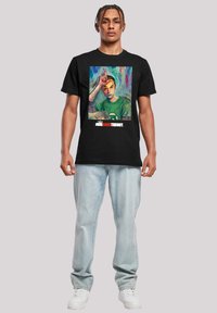 Camiseta negra de algodón con un estampado gráfico colorido de un personaje, con texto blanco abajo que dice "LA TEORÍA DEL BIG BANG." Jeans de mezclilla claros y zapatillas blancas.