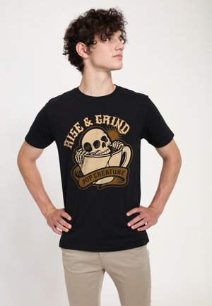 Schwarzes Baumwoll-T-Shirt mit einem grafischen Design eines Schädels und einer Kaffeetasse, versehen mit dem Text "RISE & GRIND" in Beige- und Goldtönen.
