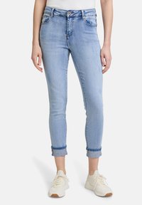 Ljusblå denimjeans med slim fit, uppvikta fållar och framfickor. Tyget visar lätt slitage för textur. Parat med vita sneakers.