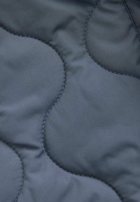 Tissu matelassé bleu marine avec un motif circulaire, présentant une texture lisse et une couture contrastante. Matériau léger et résistant à l'eau.