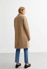 Beige wollen blend jas met een klassieke kraag, lange mouwen en een rechte snit, gecombineerd met lichtblauwe jeans en zwarte platte schoenen.