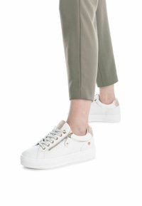 Zapatillas blancas con paneles de cuero texturizado, detalles en beige, ojetes dorados y cierre. Combinadas con pantalones cortos verde oliva.