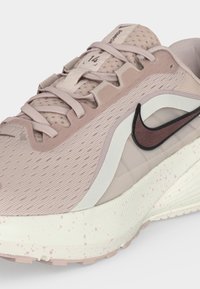 Ανοιχτό ροζ παπούτσι για τρέξιμο Nike με επάνω μέρος από δίχτυ, λευκή σόλα με ροζ στίγματα και σκούρο λογότυπο Nike στο πλάι.