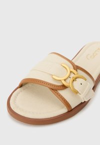 Beige canvas slide sandal with brown leather accents, featuring a gold metal buckle detail and cushioned insole for comfort.