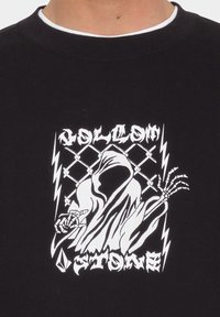 Sudadera negra con un destacado diseño gráfico blanco de una figura en capa con manos esqueléticas, rayos y el texto "VOLCOM STONE."