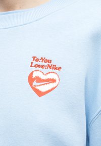 Ανοιχτό μπλε ύφασμα με κόκκινο κείμενο "Προς: Εσένα Αγαπώ: Nike" πάνω από μια κόκκινη καρδιά που περιέχει το λευκό λογότυπο Nike swoosh.