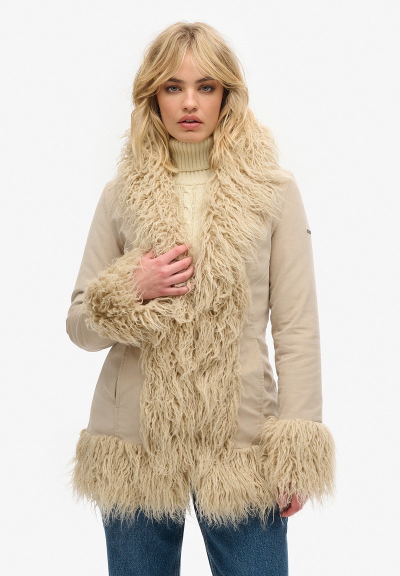 Beige jas met een getextureerde, harige nep-fur rand langs de kraag, mouwen en zoom. Glad stoffen lijf met een getailleerd ontwerp.