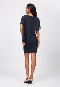 Marinblå klänning med en svävande chiffongöverdrag, figursydd bodycon-design, knälång, slät textur, i kombination med öppetåiga klacksandaler.