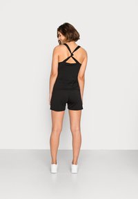 Topo de tanque preto com alças cruzadas nas costas, combinado com calções pretos. Os materiais parecem leves e com uma textura suave, apresentando um design simples.