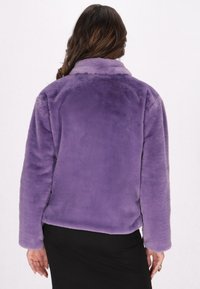 Giacca in pelliccia sintetica viola con colletto, vestibilità rilassata e maniche lunghe. La texture è morbida, senza hardware visibile o motivi.