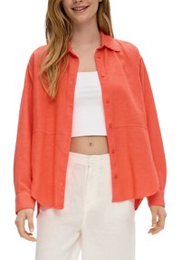 Koraalrode button-up shirt, relaxed fit, lange mouwen, kraag, met twee borstzakken; gecombineerd met witte high-waisted broek.