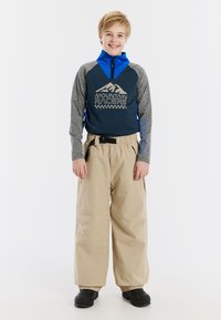 Blauwe en grijze zip-up top met bergafbeelding, gecombineerd met beige sneeuwbroeken, met een elastische tailleband en zakken.