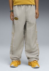 Jasno beżowe spodnie wide-leg z elastycznym paskiem, żółtymi lamówkami i bocznymi kieszeniami. Noszone z jaskrawożółtymi sneakersami.