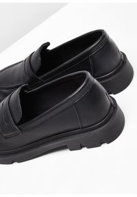 Mocassins en cuir noir avec un design épuré, un bout arrondi, une tige texturée et une semelle en caoutchouc épaisse, agrémentés de détails de surpiqûre discrets.