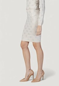 Jupe longueur genou, ajustée, de couleur beige clair avec une texture lisse, présentant un motif diamant subtil et des accents de logo.