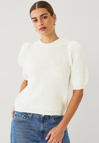 Maglione bianco lavorato a maglia con maniche a sbuffo corte, tessuto testurizzato, collo e orlo a coste, abbinato a jeans in denim blu.