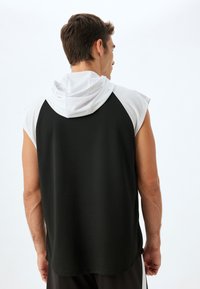 Top senza maniche con cappuccio bianco, corpo nero e tessuto testurizzato. Presenta una vestibilità comoda e un design pulito senza decorazioni.